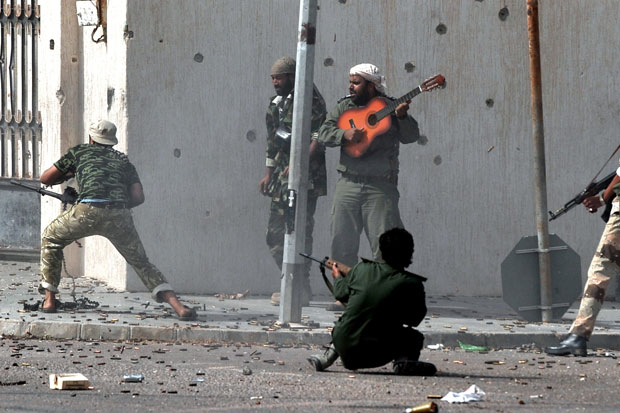 Libya's new regime forces fire their weapons at fighters loyal to Colonel Gaddafi as a comrade plays a guitar during a battle in Sirte on October 10, 2011, (Photo credit: ARIS MESSINIS/AFP/Getty Image