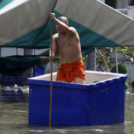 A monk paddles through a flooded temple complex in Nonthaburi province (Reuters)