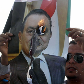An anti-Mubarak demonstrator burns a picture of former Egyptian president Hosni Murbarak in front of the police academy where his trial is taking place in Cairo 