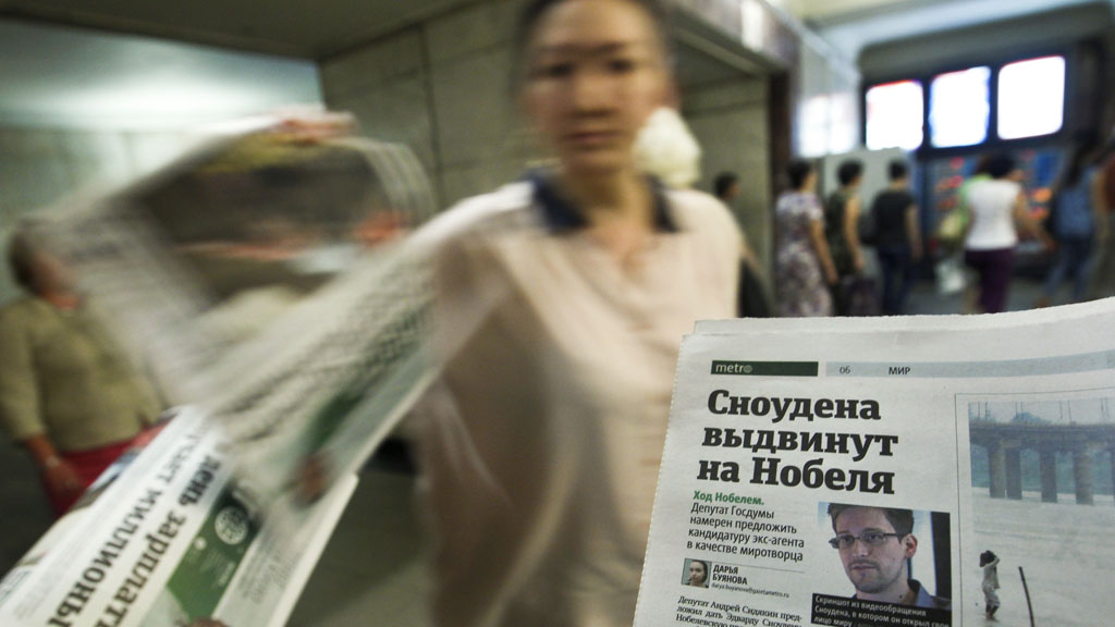 An employee distributes newspapers, with a photograph (R) of former U.S. spy agency contractor Edward Snowden