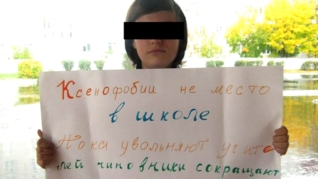 Maria Novikova holds a banner which says 'There is not place for xenophobia in schools. While teachers are sacked, bureaucrats cut the budgets'