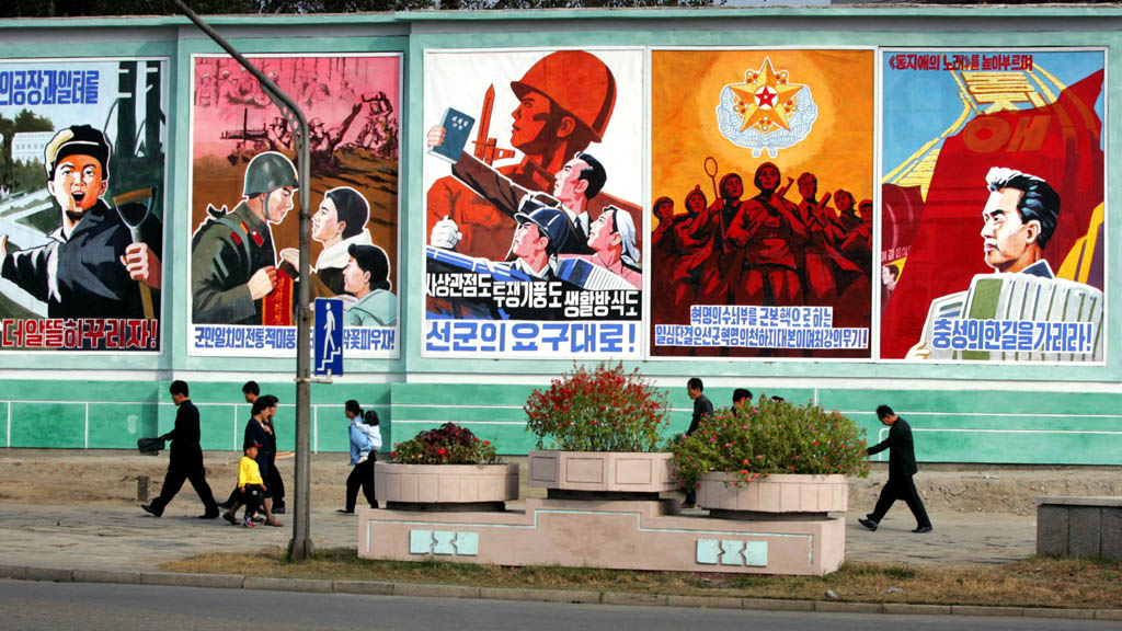 North Koreans walk in front of propaganda posters in North Korea's capital Pyongyang