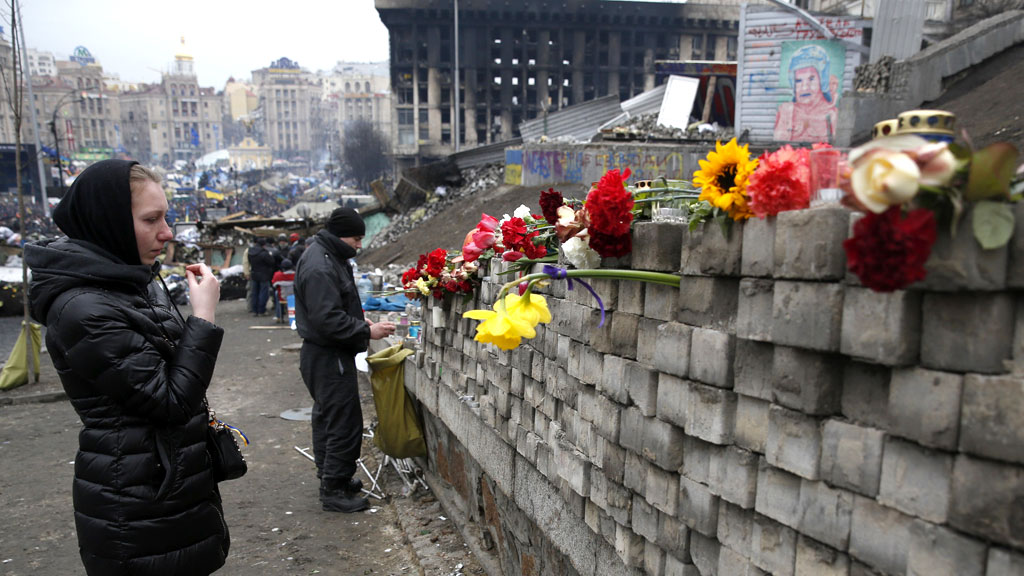 A woman makes the sign of the cross in front of a flower covered wall in Independence Square, Kiev. 