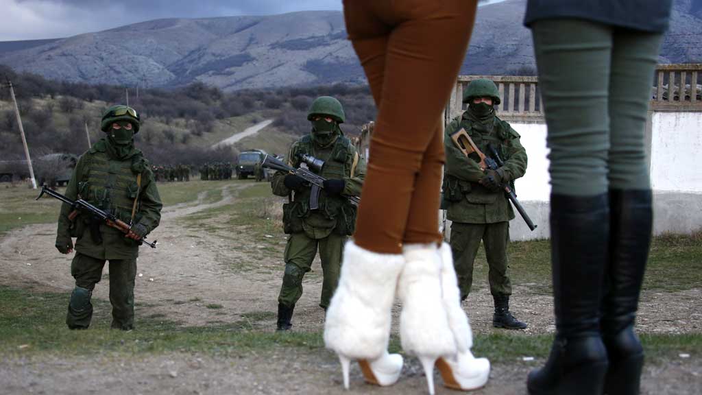Local women watch armed men, believed to be Russian soldiers, assemble near a Ukrainian military base in Perevalnoe (R)