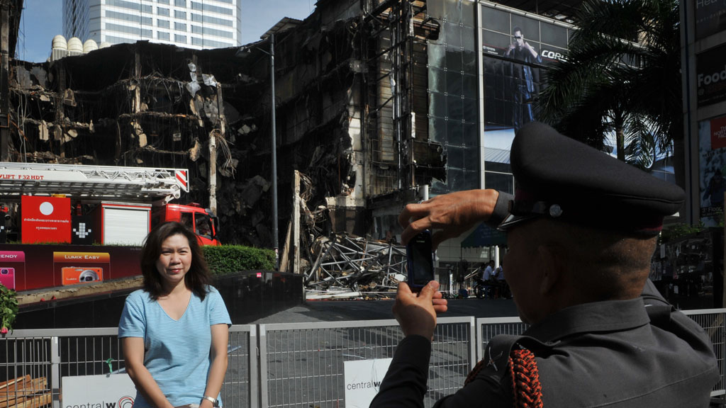 A woman has her photograph taken in front of burnt out CentralWorld mall in Bangkok in 2010