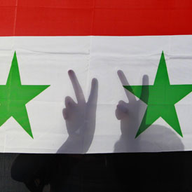 A Syrian protester gestures victory signs behind their national flag aduring a protest in front of the Syrian embassy in Amman (Reuters)