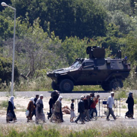 Syrian refugees walk past Turkish forces in Hatay (Reuters)