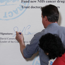 David Cameron signs his NHS pledge during the General Election campaign (R)