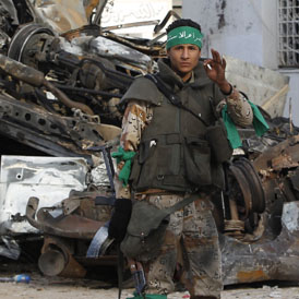 A Libyan army soldier smokes in front of destroyed vehicles near a damaged mosque at Martyr's Square in the centre of Zawiyah (Reuters)