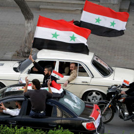 Syria: supporters of President Bashar al-Assad wave their national flag as they drive around in vehicles with his pictures in the Old City of Damascus (Getty)