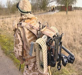 A soldier walks with a Dragon Runner IED robot strapped to his backpack.