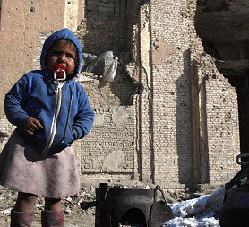 A displaced Afghan boy stands in front of damaged building (credit: Reuters)